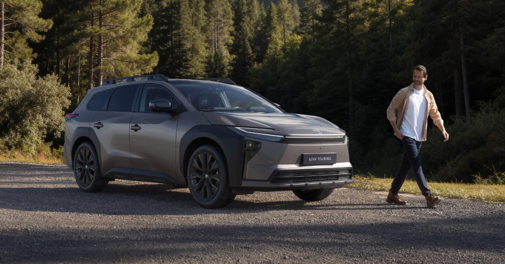 Veículo Toyota bz4X Touring parado num ambiente rural com uma pessoa a passear e olhar para o carro