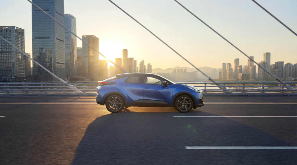vista lateral de um veículo azul da toyota a andar numa ponto no pôr do sol e prédios no fundo