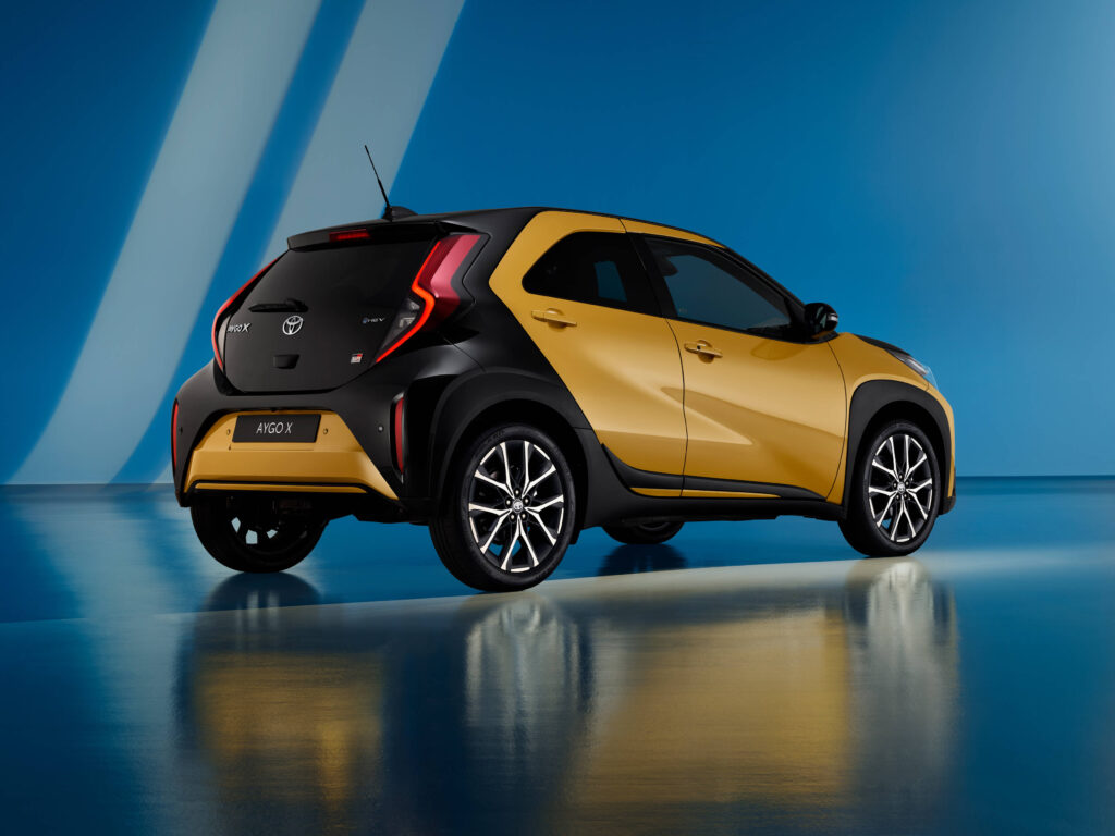Perspetiva 3/4 traseira do novo Toyota Aygo X GR Sport, sob um fundo azul e com o piso a refletir o veículo