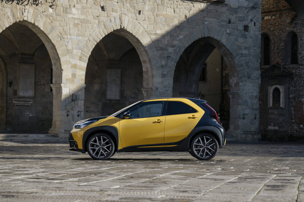 Vista lateral do novo Toyota Aygo X Hybrid sob um fundo histórico urbano