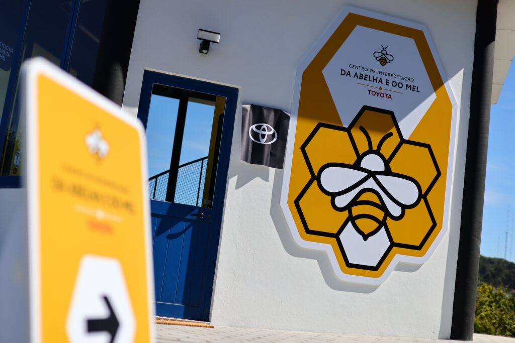Close up da entrada do Centro de Interpretação da Abelha e do Mel, com placa com nome e logótipo do centro, bem como o logótipo da Toyota, em destaque